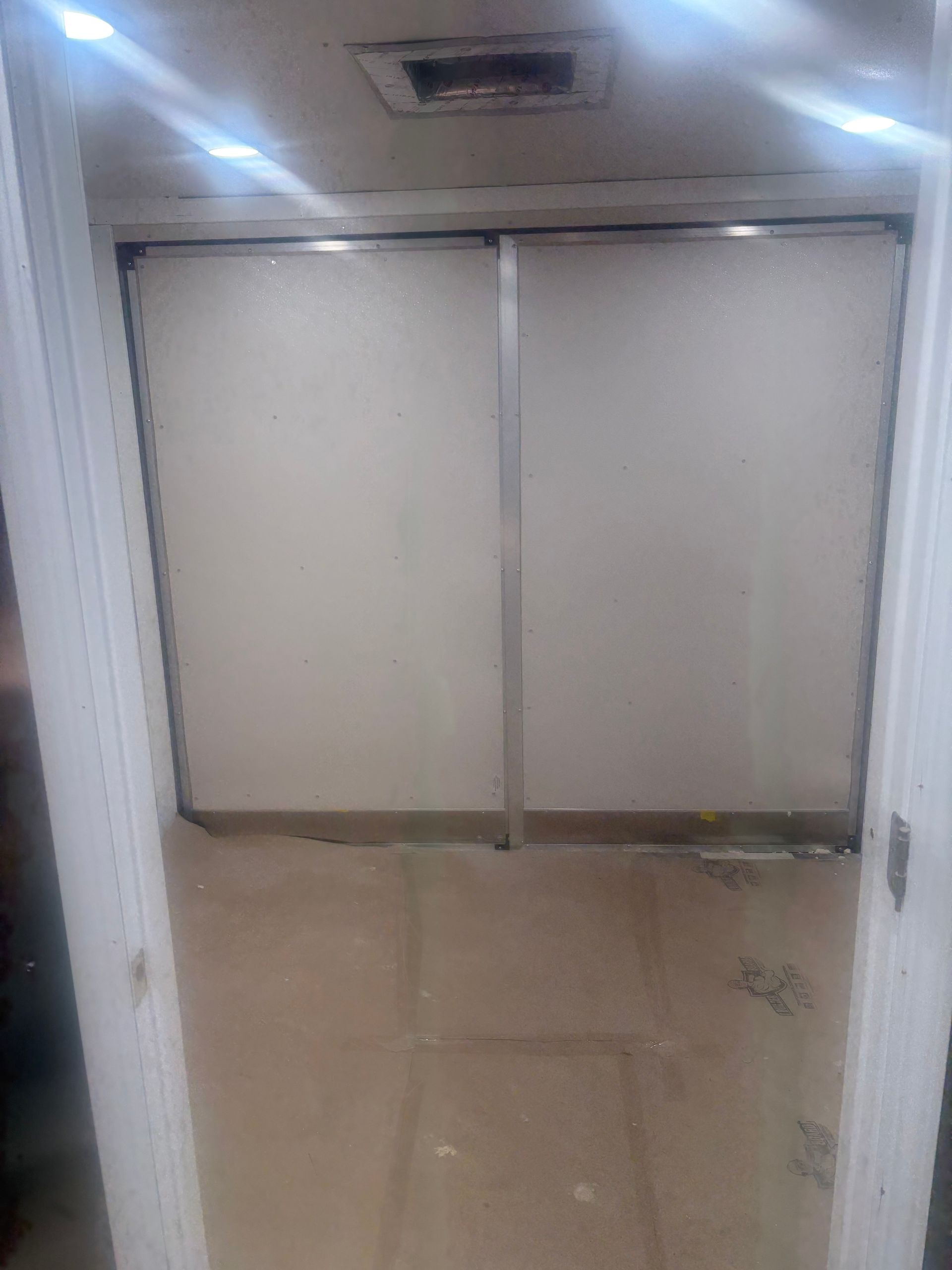 White sliding closet doors with silver frames set in a doorway, with a beige floor covered in protective paper.