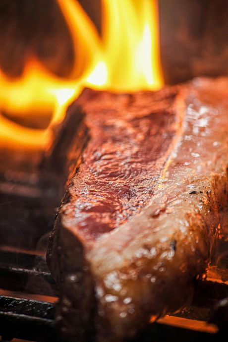 A raw steak searing on a hot grill with flames rising in the background.