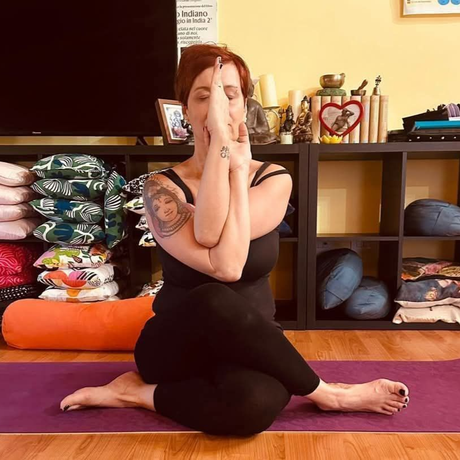 Una persona esegue una posizione yoga seduta su un tappetino viola.