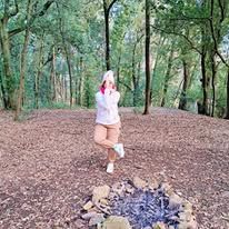 Una persona con una felpa rosa con cappuccio si trova in una foresta vicino a un piccolo falò.
