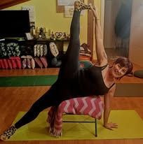 Una persona esegue una posizione yoga, in equilibrio laterale su una sedia con una gamba sollevata, in un soggiorno.