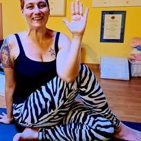 Una donna sorridente seduta a gambe incrociate su un tappetino da yoga, alza una mano in uno studio.