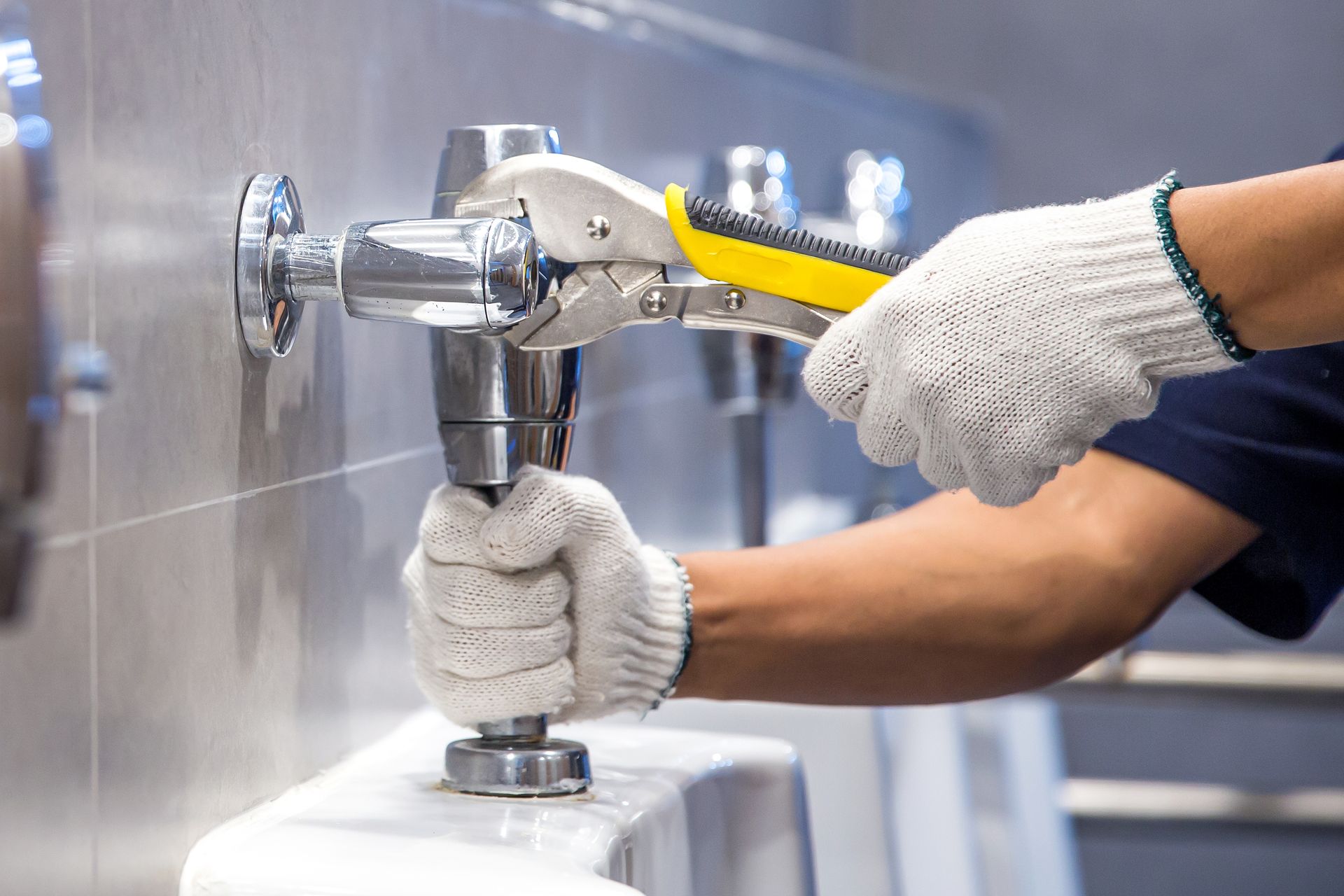 A person wearing gloves using pliers to repair a urinal in a restroom.