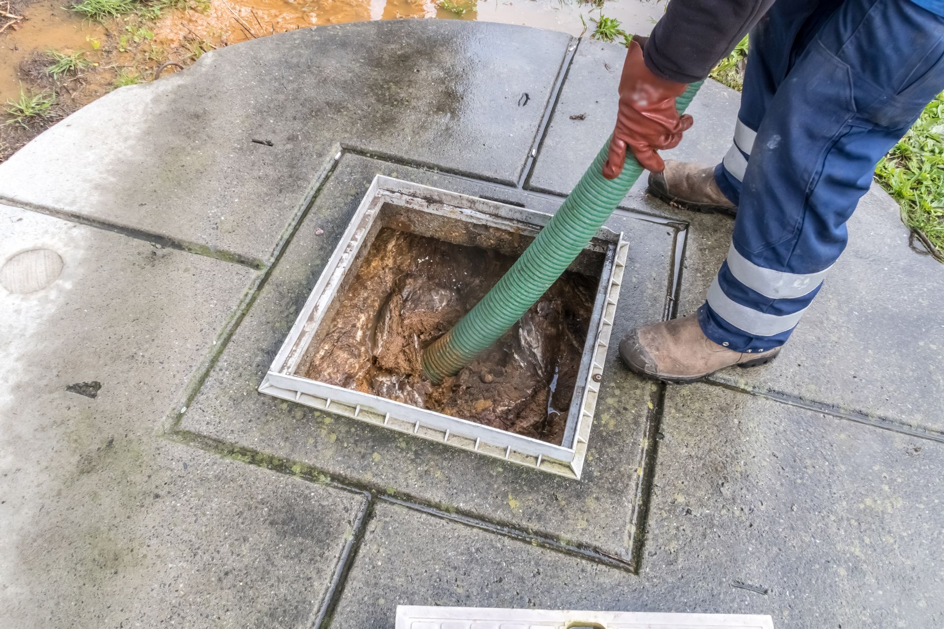 Person in work clothes pumping waste from a square concrete access point; outdoors.