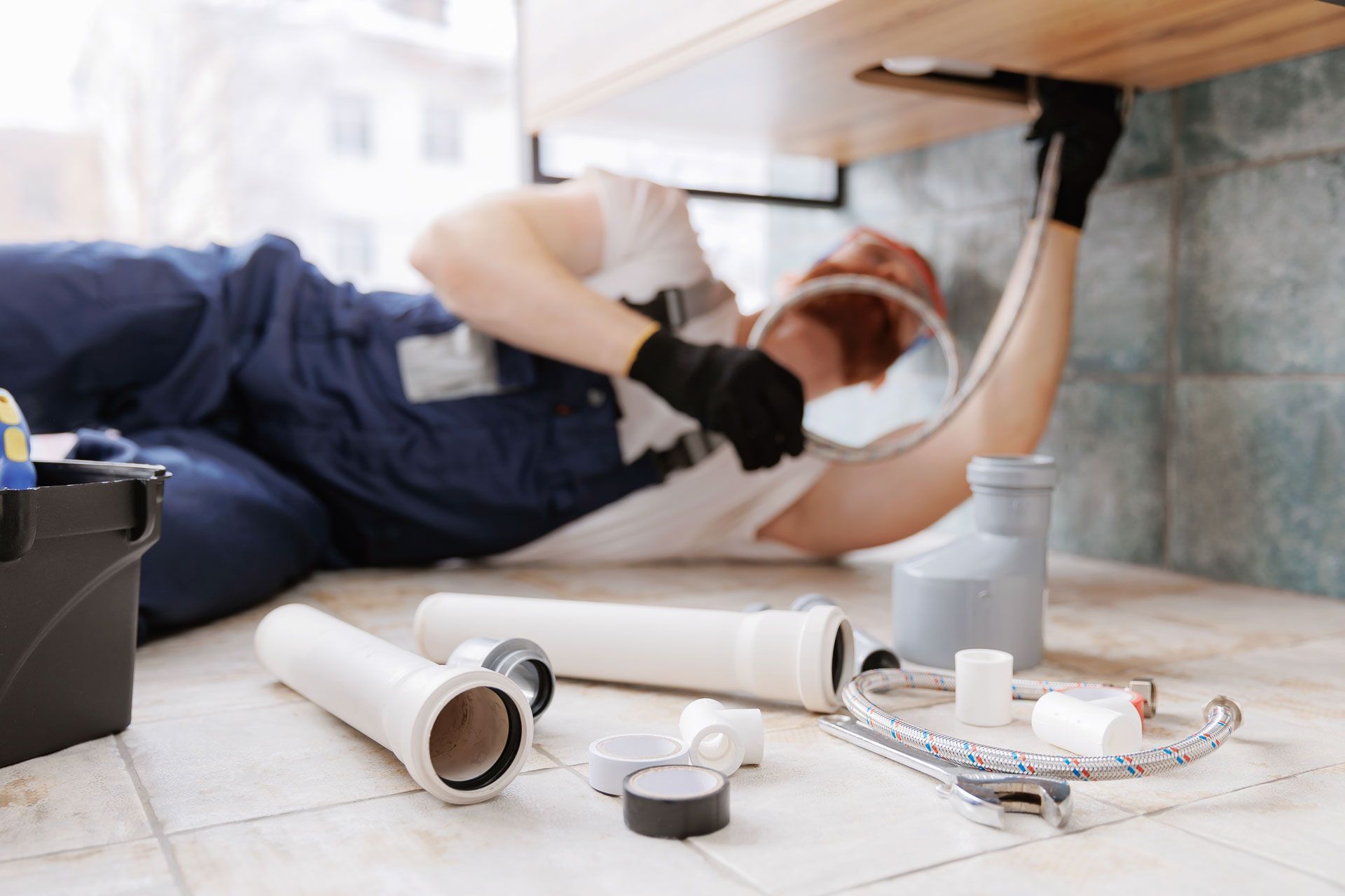 Plumber fixing a sink under a countertop with tools and pipes on the floor