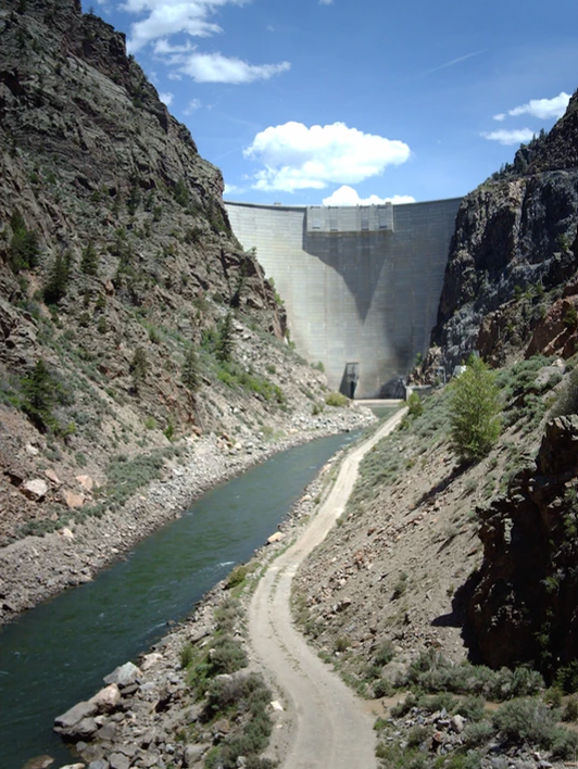 A river flowing through a canyon with a dam in the background