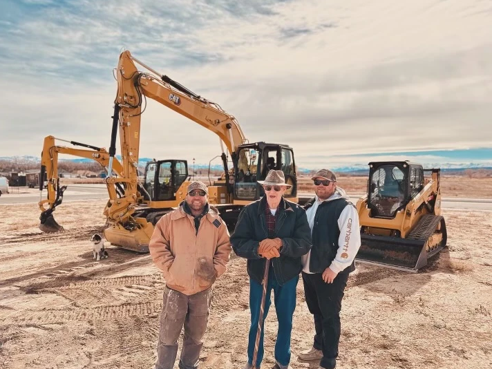 Three men are standing in front of a bulldozer and an excavator.