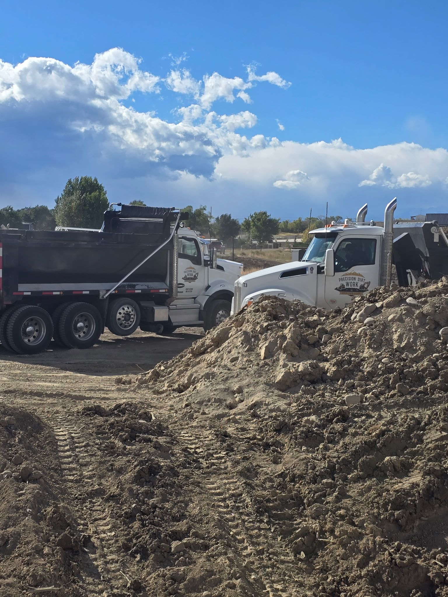 Two dump trucks on dirt under a blue sky, likely at a construction site.