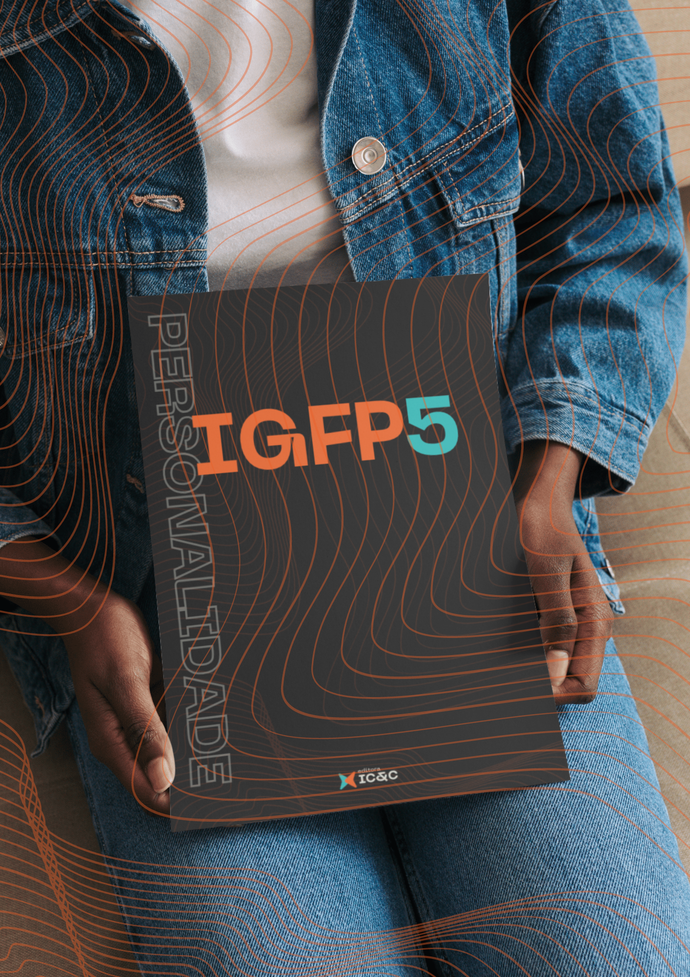 Pessoa segurando um livro preto do IGFP5 com texto laranja, vestindo jaqueta jeans e calça jeans.