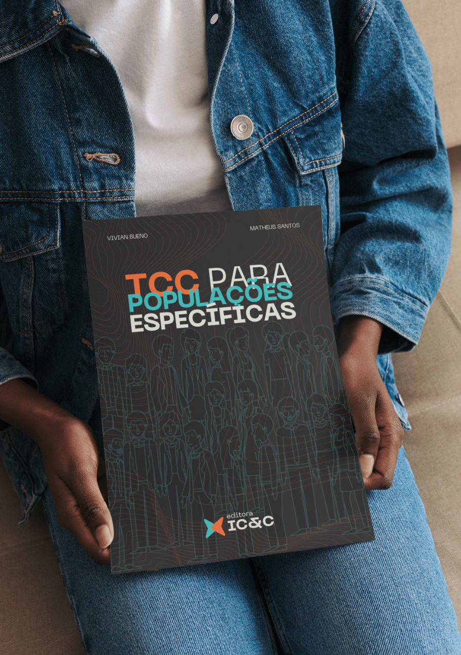 Person holding a black booklet titled “TCC para populações específicas” on a denim-clad lap