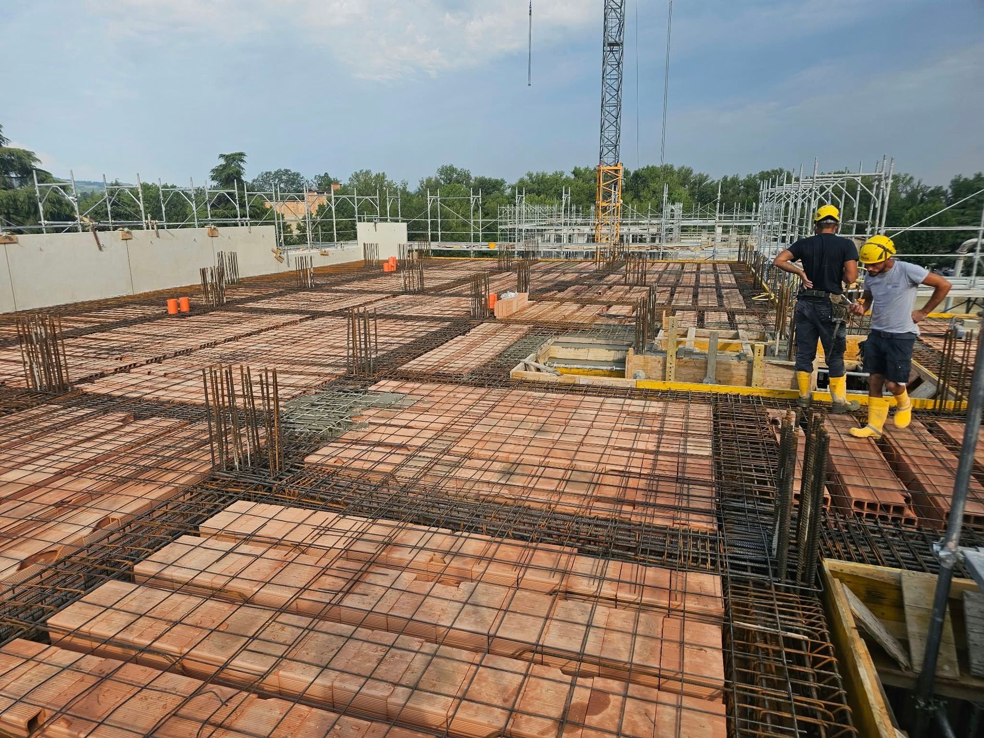 Operai edili su una soletta in cemento armato e mattoni in costruzione, con impalcature e caschi di sicurezza.