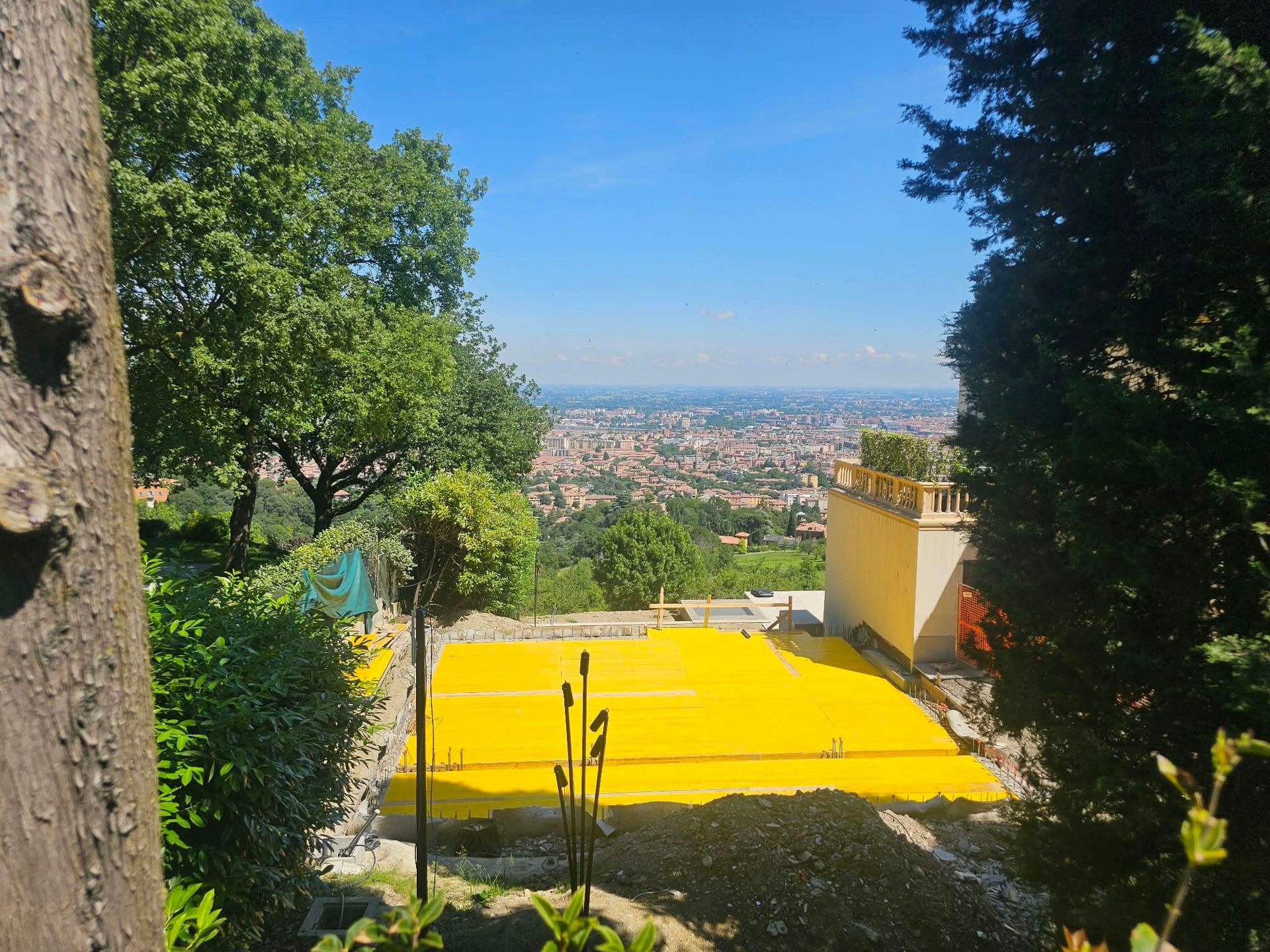 Terrazza giallo brillante con vista sullo skyline della città, incorniciata dagli alberi sotto un cielo azzurro terso.