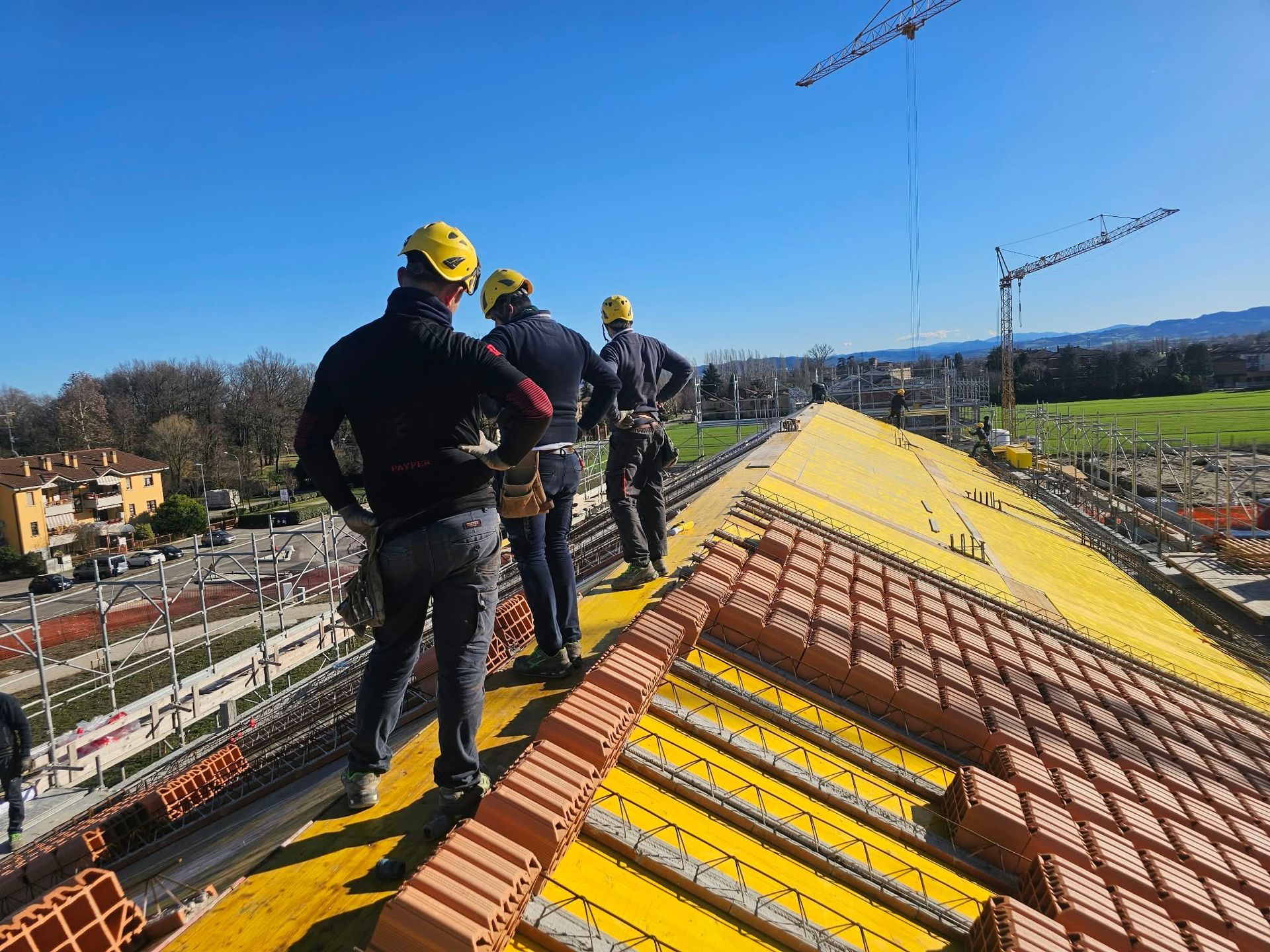 Operai con i caschi in piedi su un tetto giallo in costruzione, con gru sullo sfondo