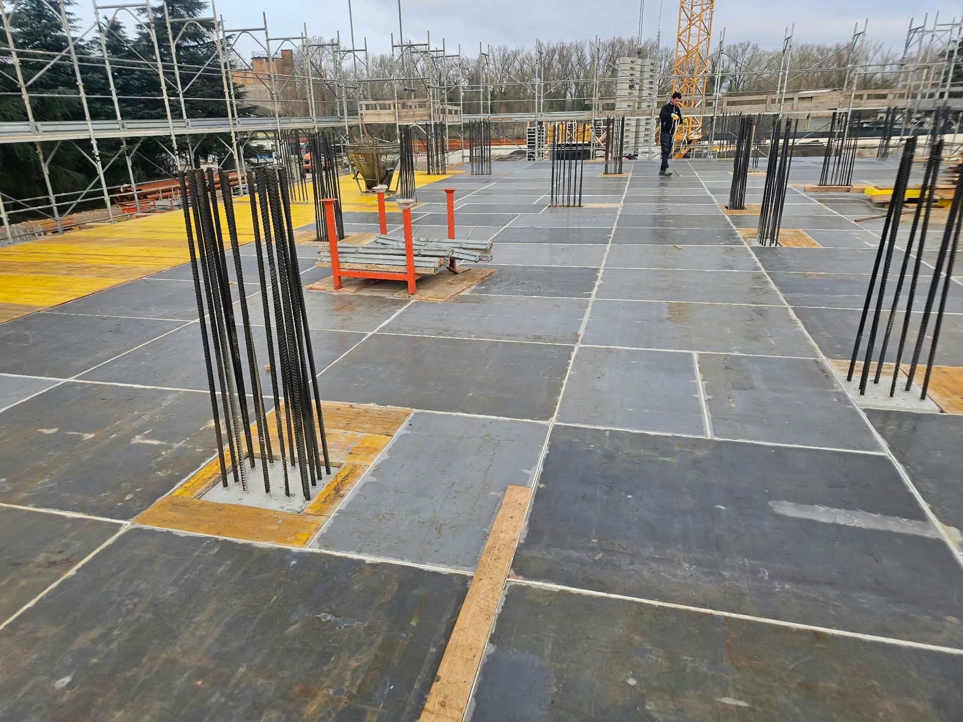 Cantiere con pilastri in armatura e solette in calcestruzzo scuro delimitate da linee di sicurezza gialle