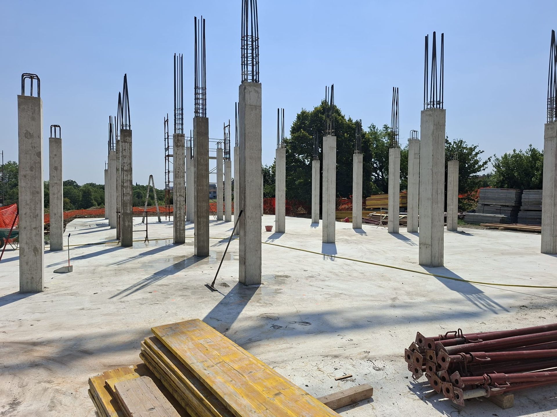Cantiere edile con colonne di cemento armato e tondini d’armatura a vista su una platea di fondazione sotto un cielo sereno