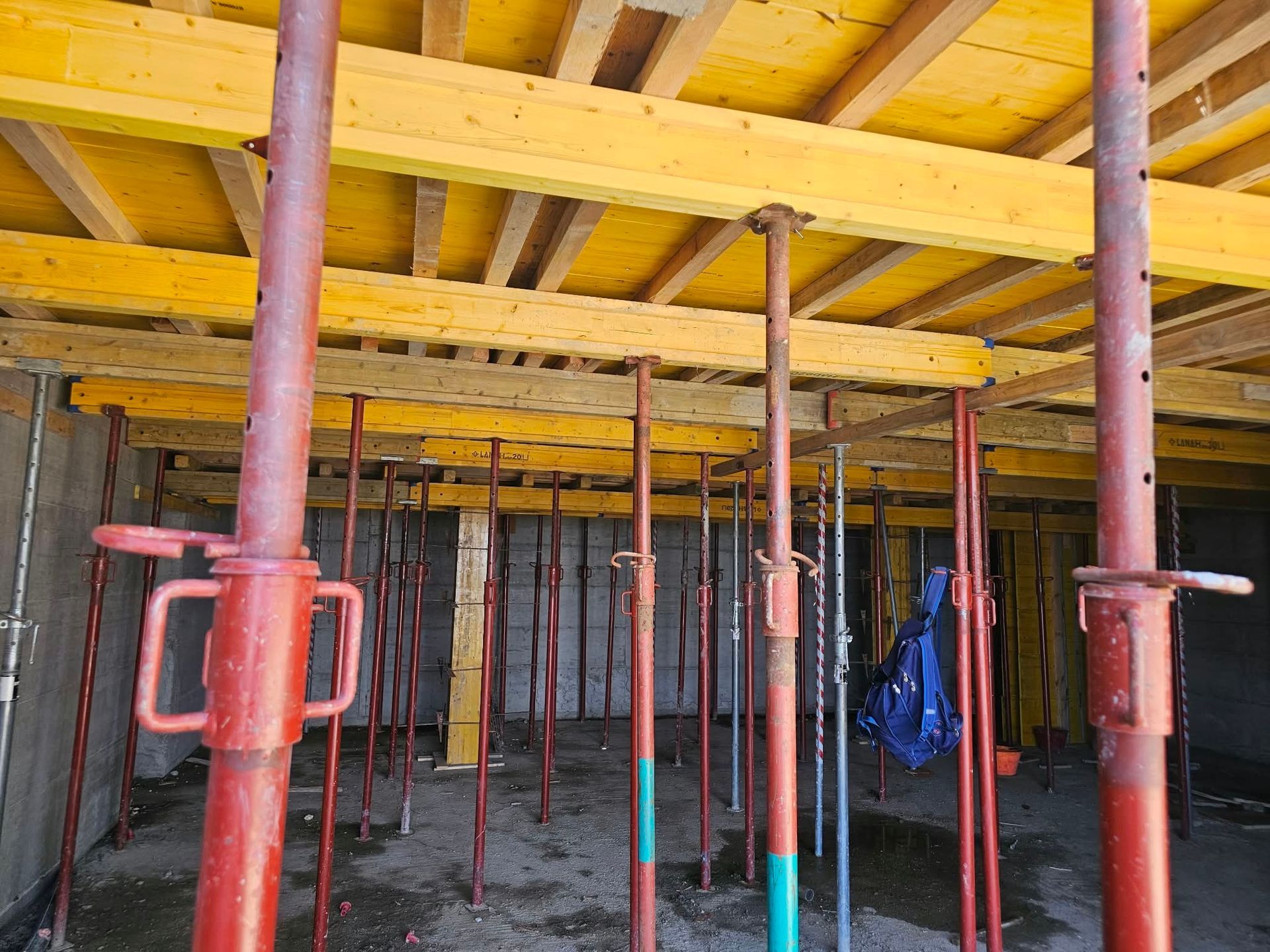 Cantiere edile in cemento con casseri gialli in alto e impalcature di sostegno rosse in basso