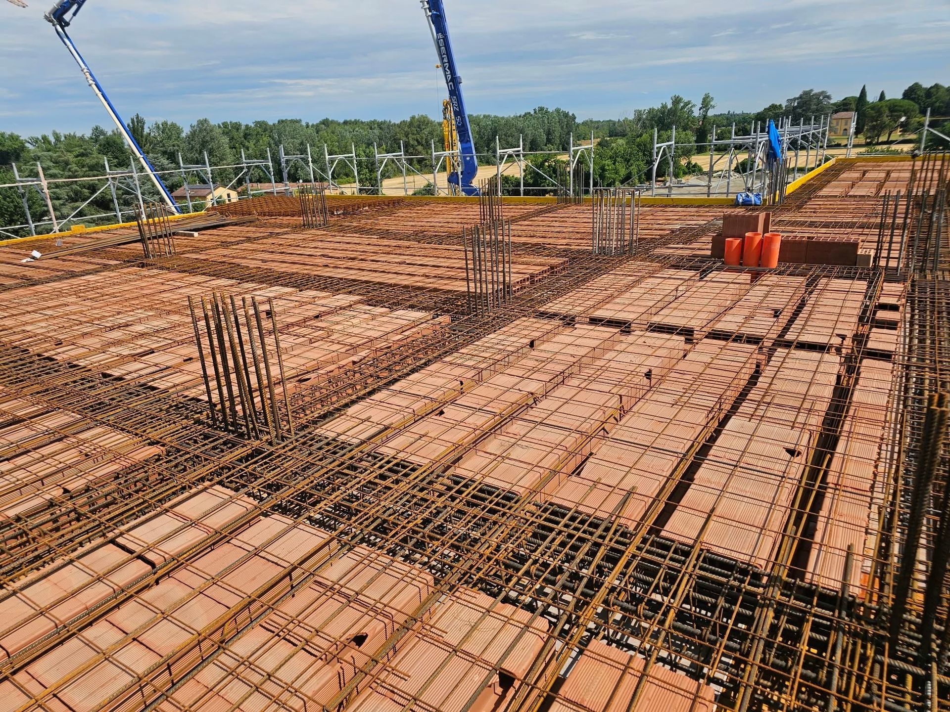 Cantiere con casseri in mattoni rossi e armatura in acciaio, visto dall’alto sotto un cielo azzurro