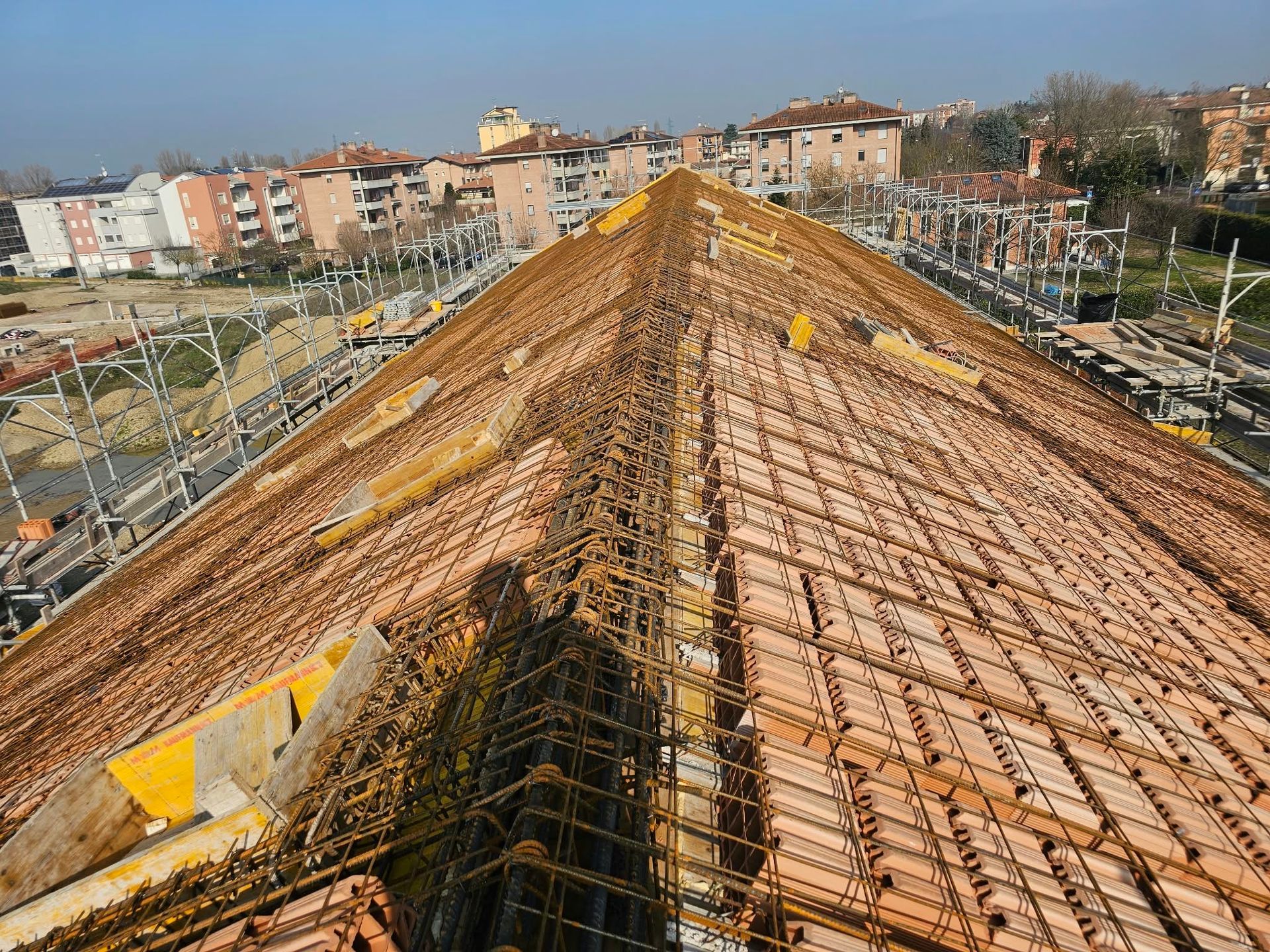 Veduta aerea di un tetto in ristrutturazione, con travi di legno a vista e gli edifici residenziali circostanti.