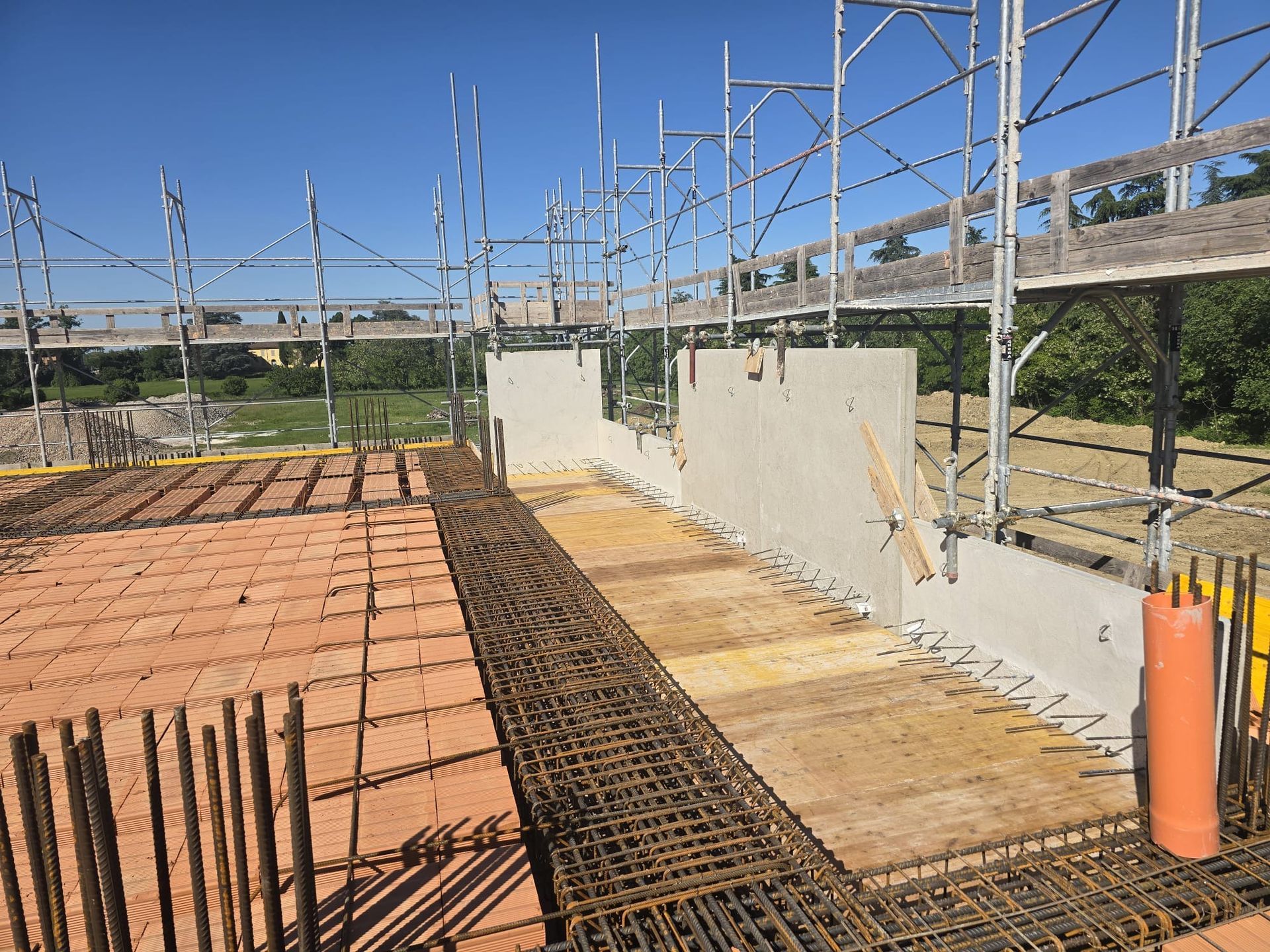 Cantiere edile con armature in acciaio, casseforme e pareti in calcestruzzo sotto un cielo azzurro