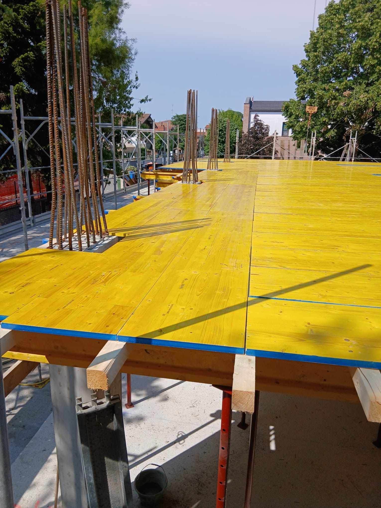 Soletta in calcestruzzo impermeabilizzata di colore giallo in un cantiere, con ferri d’armatura a vista e supporti di legno sottostanti