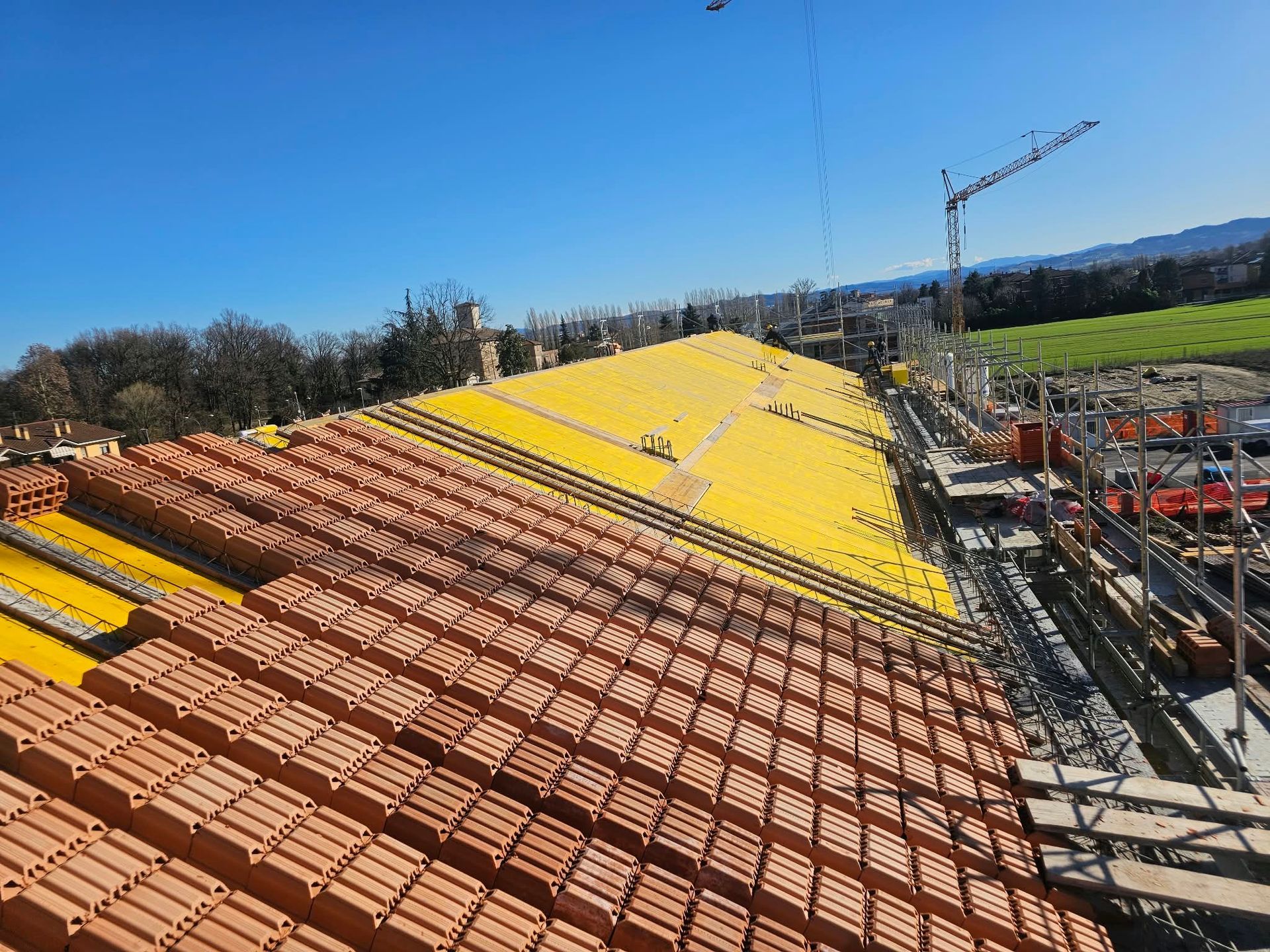 Cantiere edile con file di tegole rosse e pannelli per tetti giallo brillante sotto un cielo azzurro e sereno