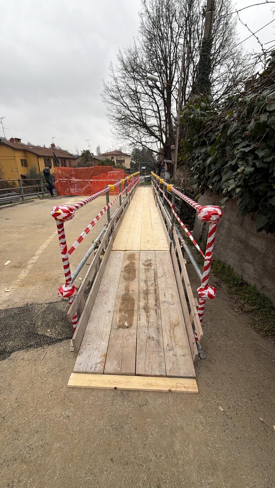 Rampa temporanea in legno su un percorso, delimitata da nastro di sicurezza bianco e rosso in un cantiere.