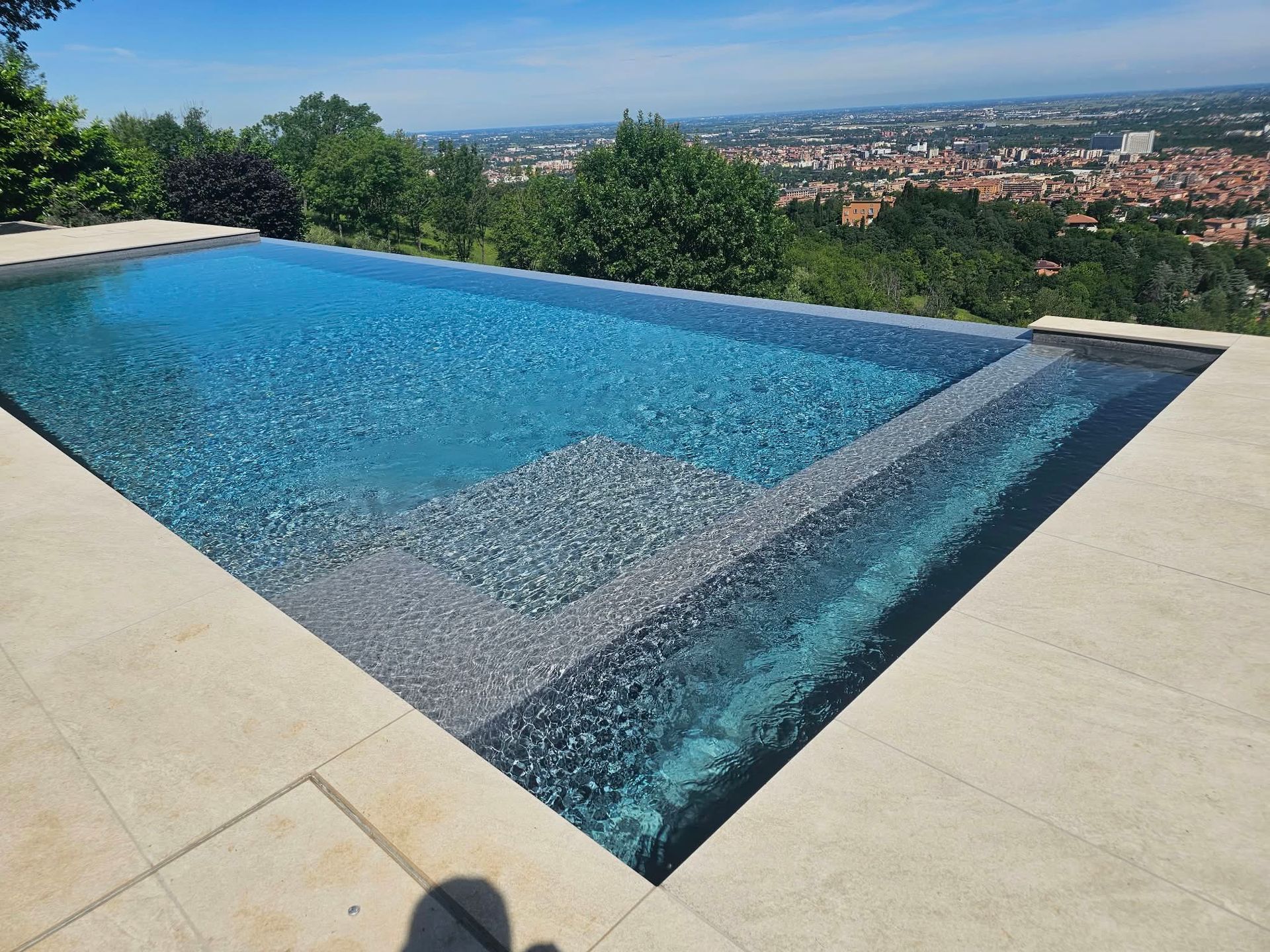 Piscina a sfioro con vista sullo skyline della città e sugli alberi, sotto un cielo sereno