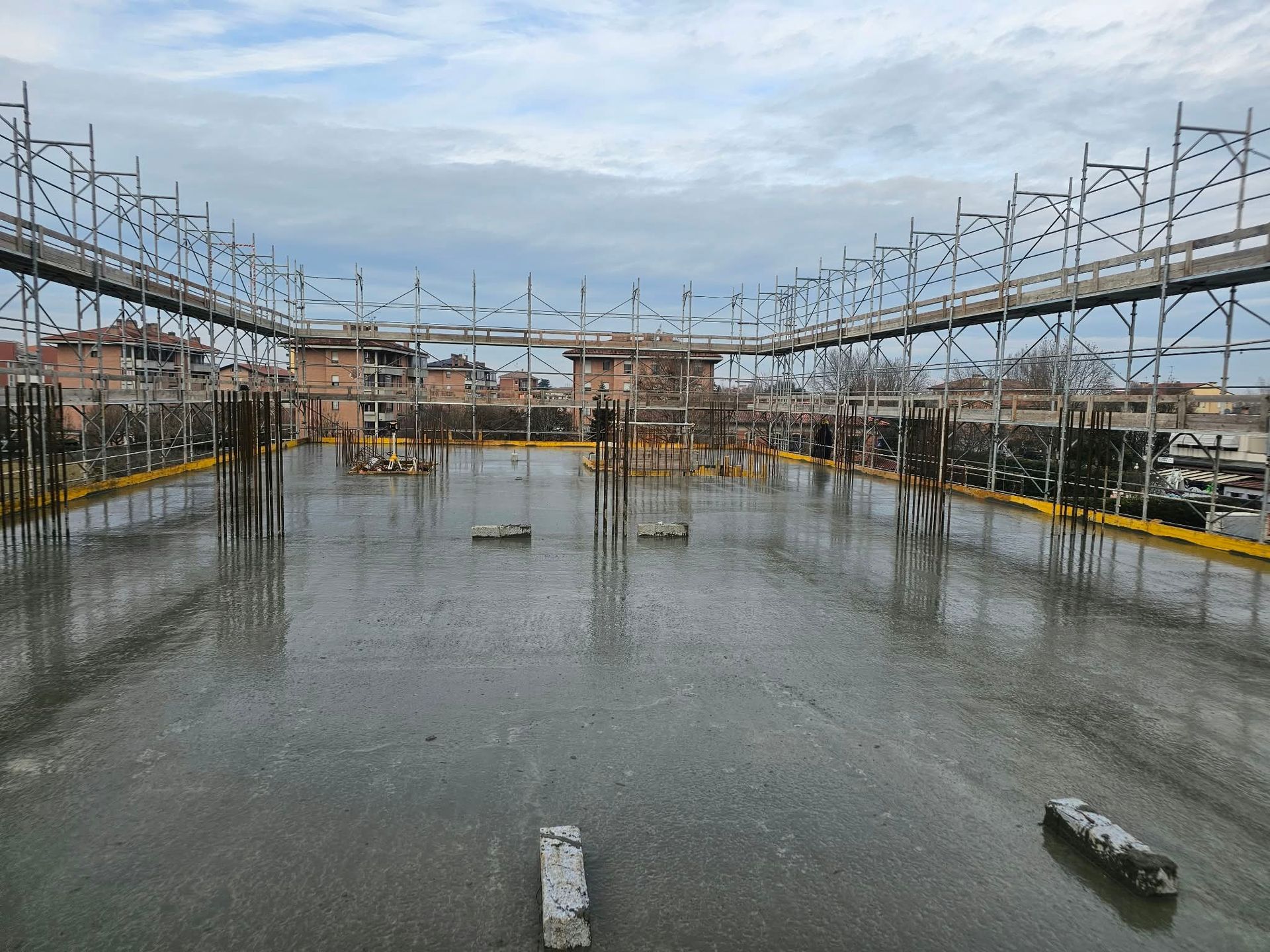 Cantiere industriale piovoso, con ponteggi attorno a fondamenta di cemento allagate
