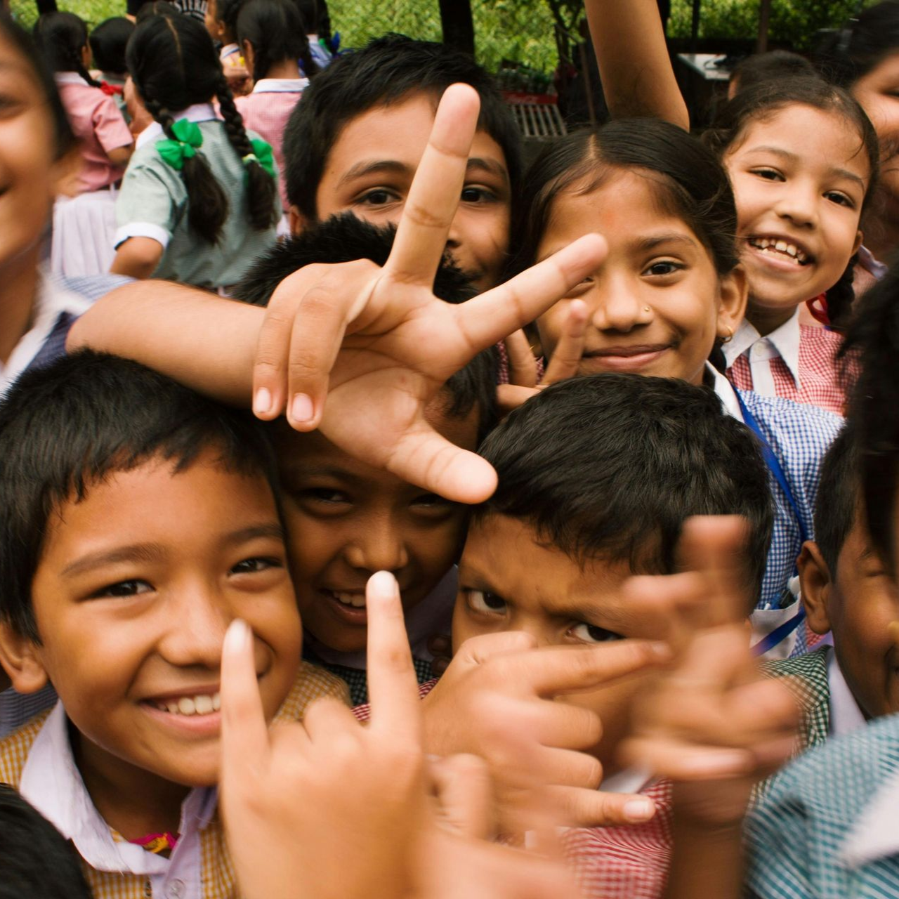 Smiling children crowded together, making hand signs and posing outdoors