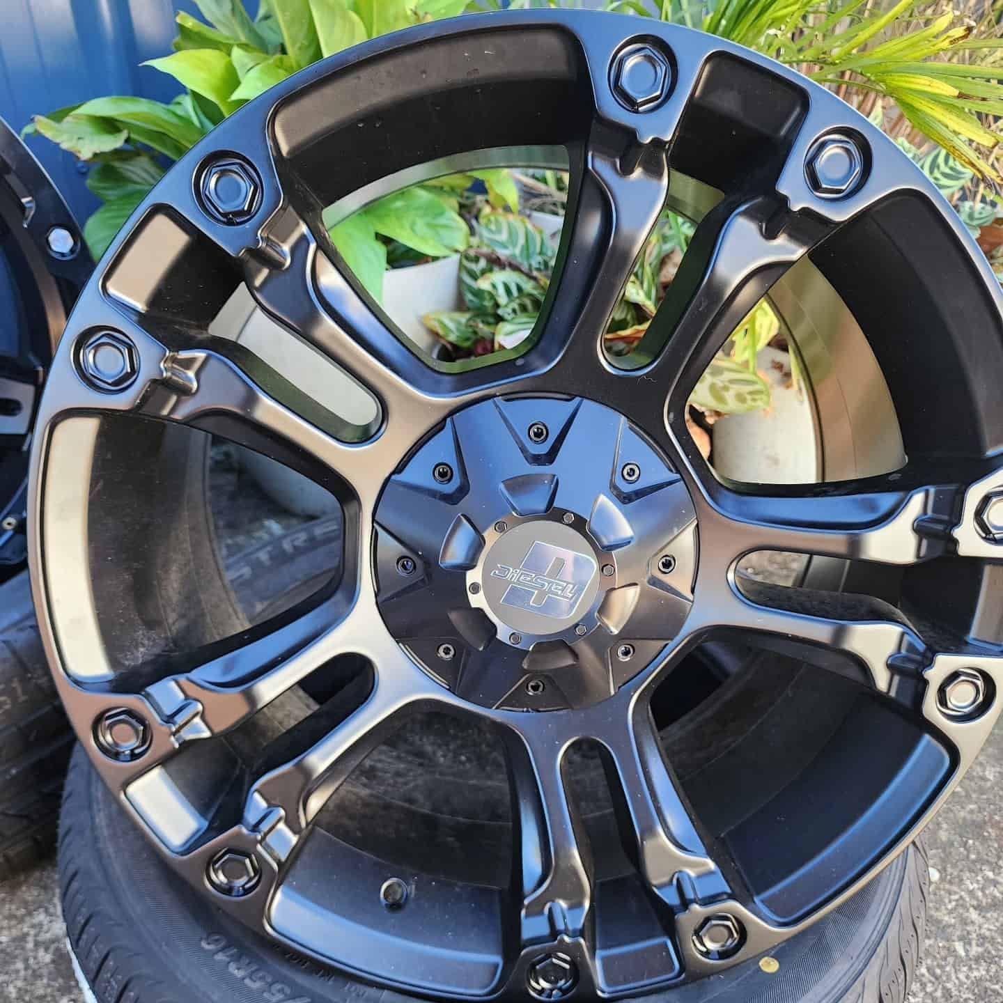 Black Alloy Car Wheel on Top of a Tyre, Surrounded by Greenery — Plateau Tyres in Wollongbar, NSW