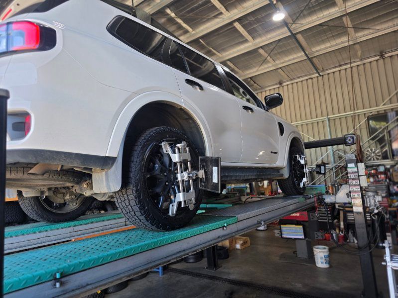 A white SUV on an automotive lift in a workshop, undergoing a wheel alignment with sensors attached to its tires.