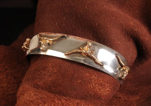 Silver and gold cuff bracelet with steer head details, resting on brown fabric.