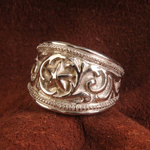 Silver ring with a star design and ornate scrollwork on a brown surface.