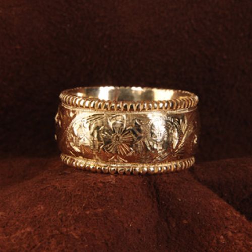Gold band ring with engraved floral design on a brown cloth.
