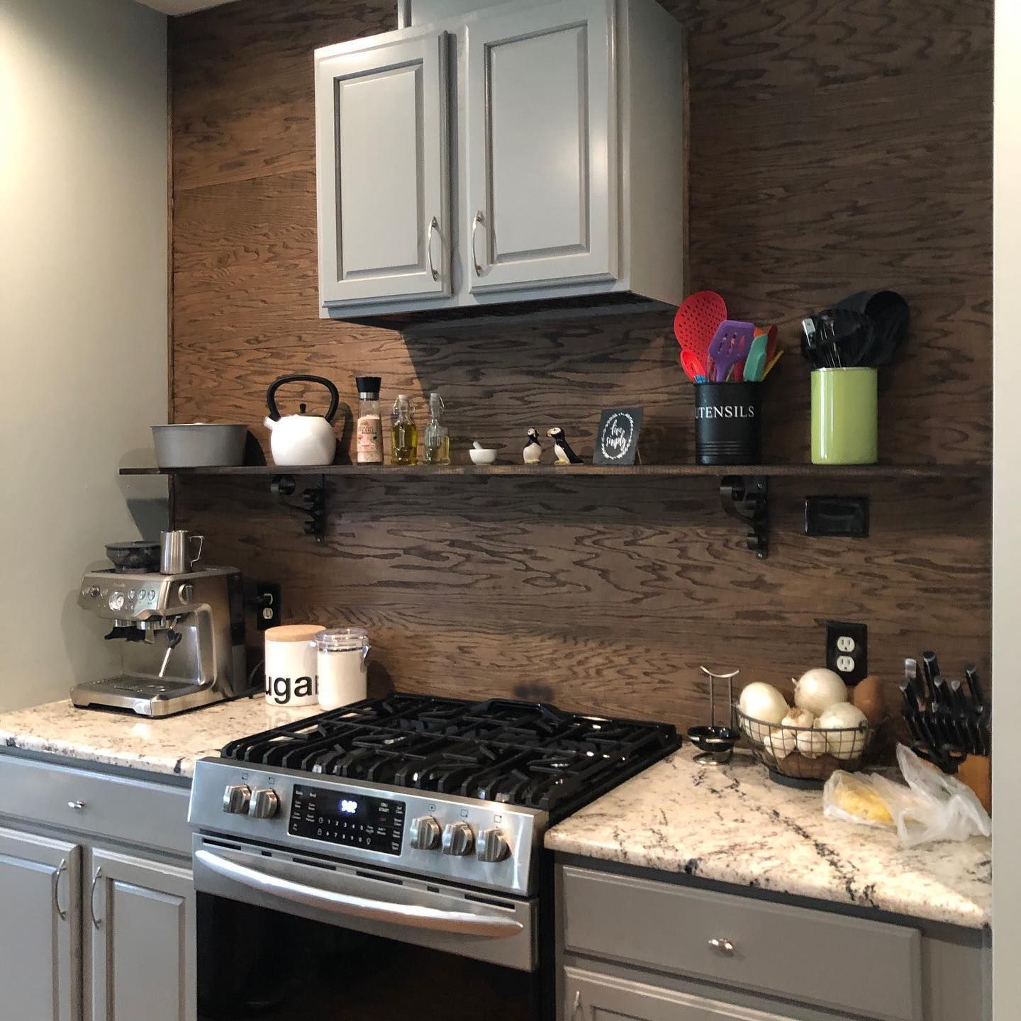 Kitchen with a gray oven, cabinets, and countertops. Brown wood backsplash with floating shelf.
