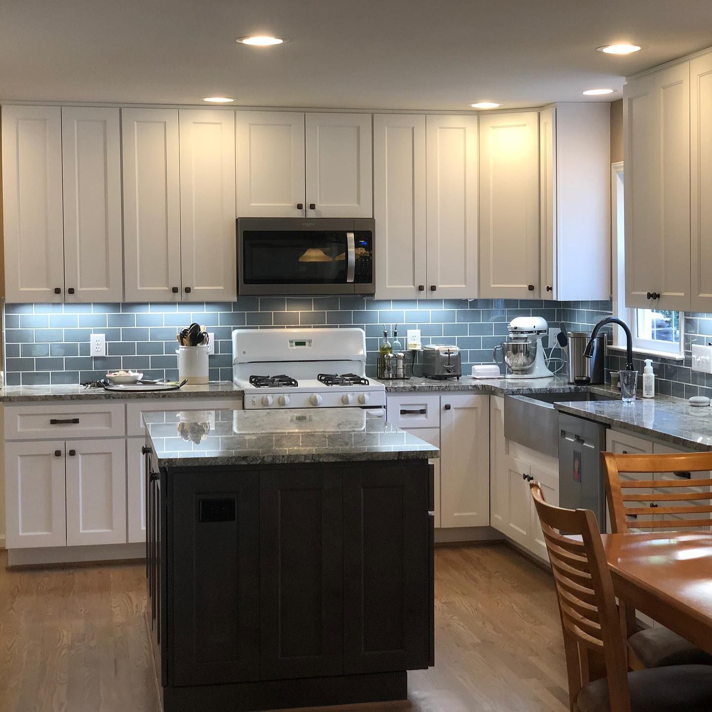Kitchen with white upper cabinets, dark island, granite countertops, and gas range.