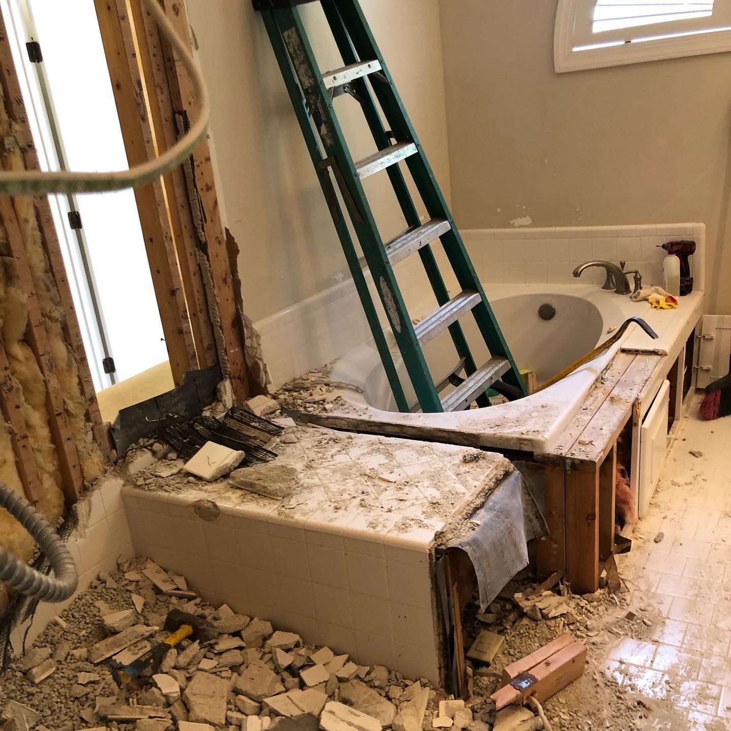 Bathroom renovation: Tub partially demolished, ladder inside, debris on floor.