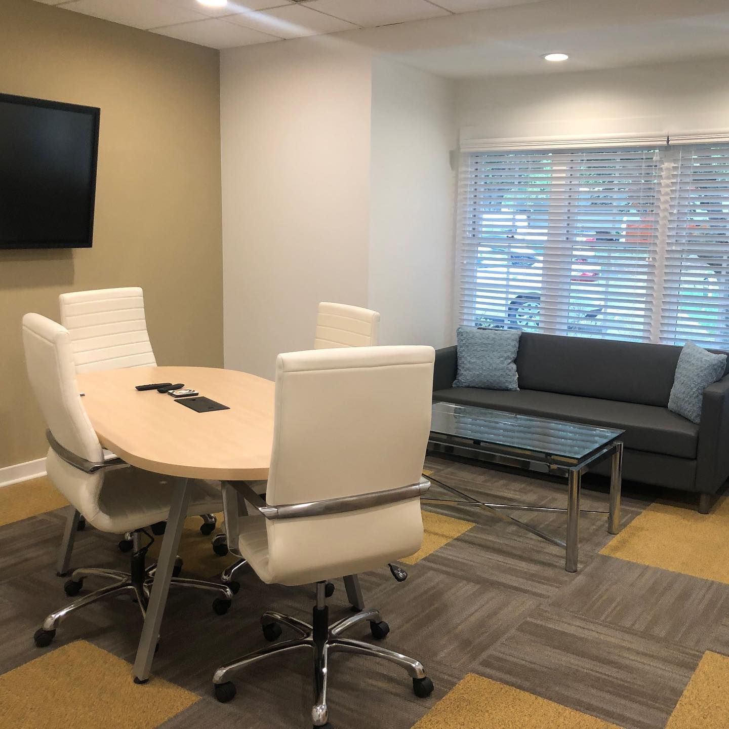 Meeting room with a table, chairs, TV, couch, and window with blinds.
