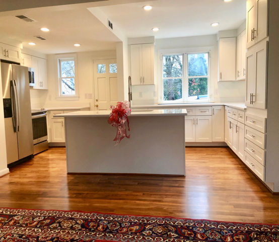 White kitchen with island, stainless steel appliances, hardwood floors, and a red rug.