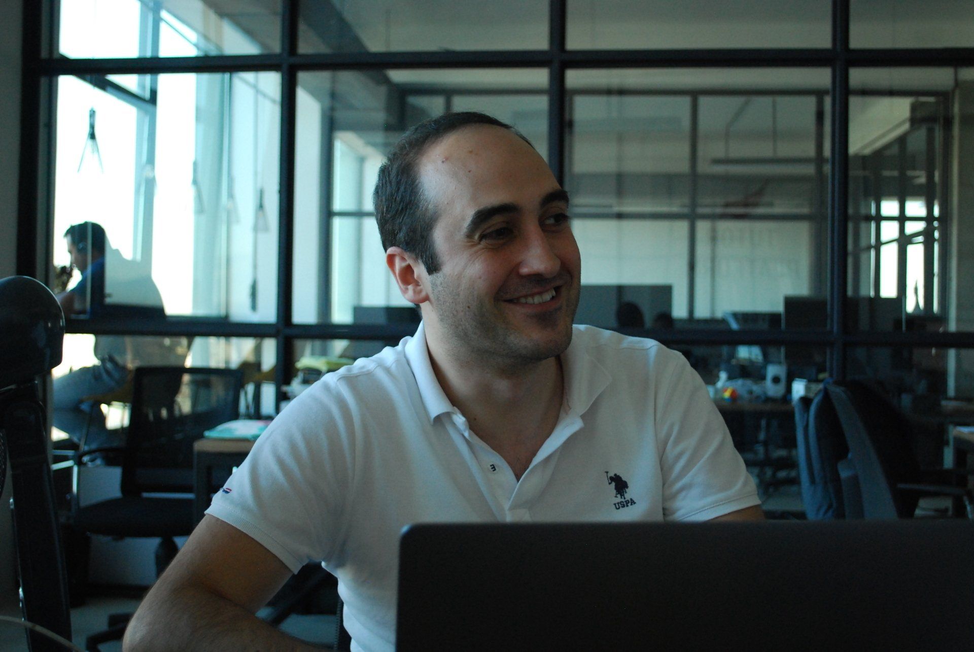 A man in a white polo shirt is sitting in front of a laptop computer.