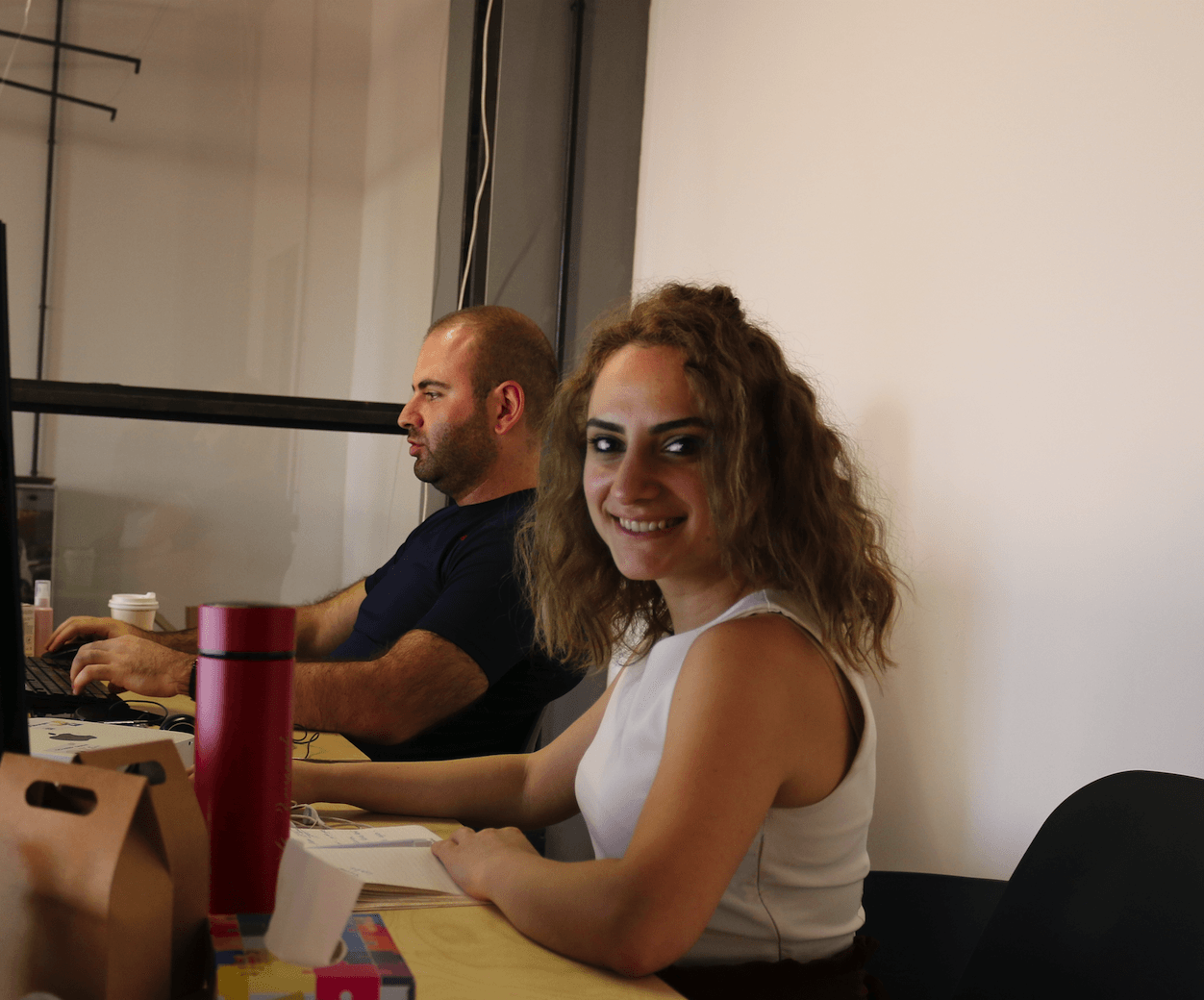 A woman in a white tank top sits at a desk next to a man in a blue shirt