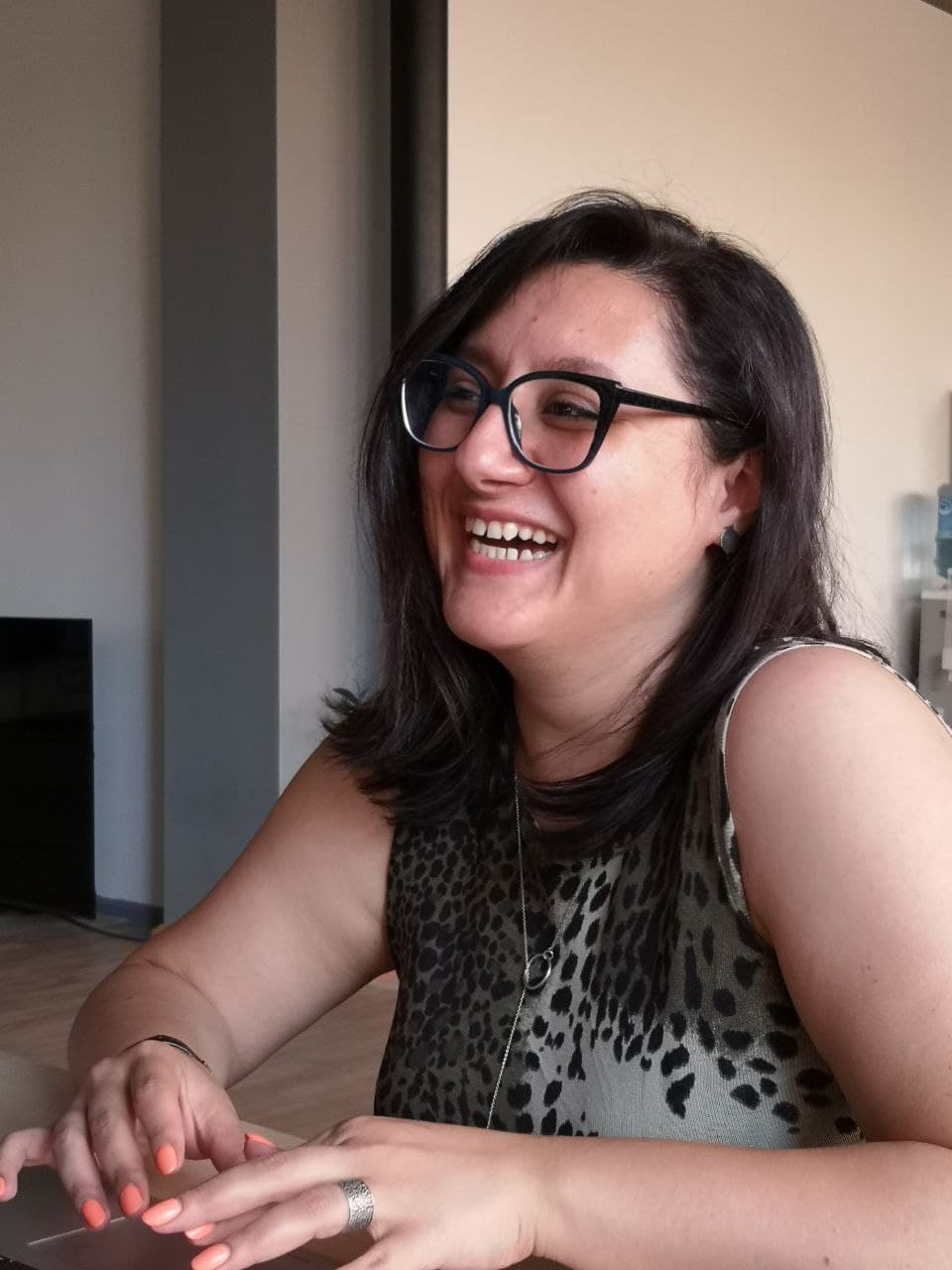 A woman wearing glasses is smiling while sitting at a table