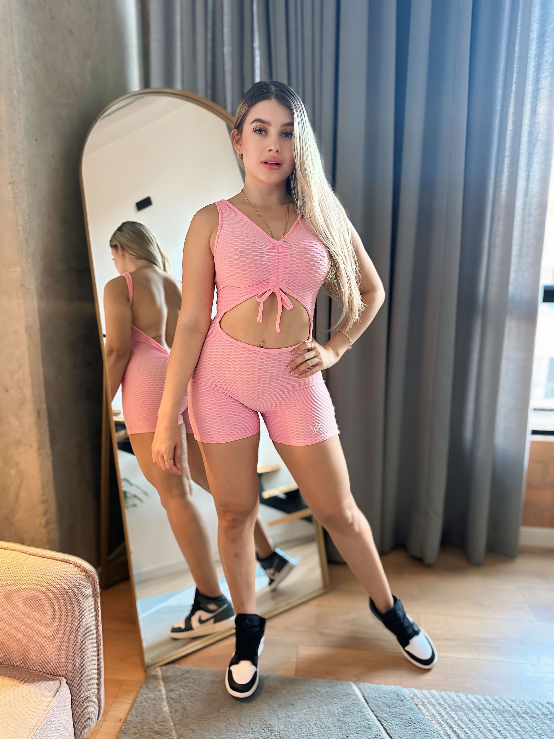 A woman in a pink crop top and shorts is standing in front of a mirror.