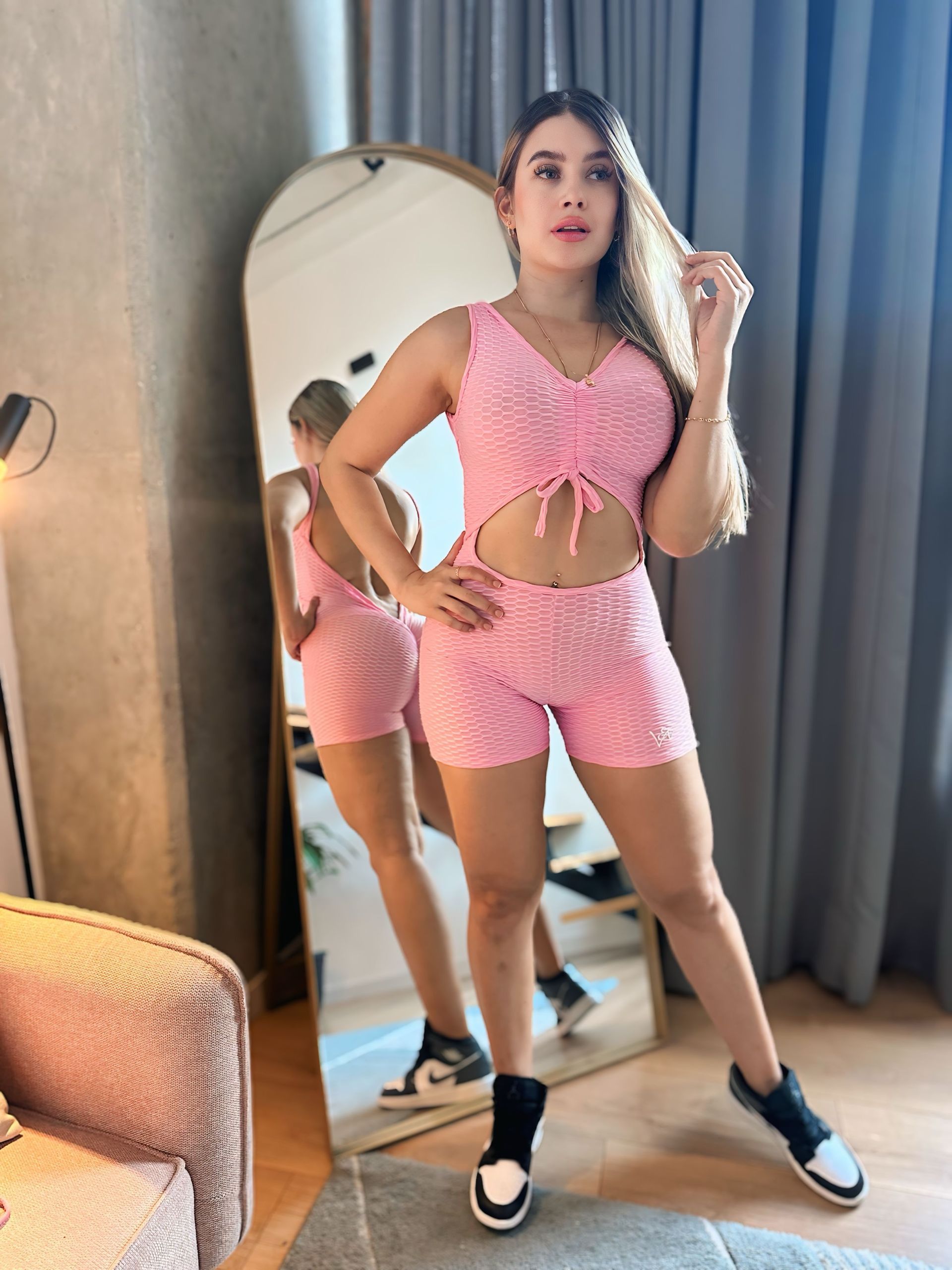 A woman in a pink crop top and shorts is standing in front of a mirror.