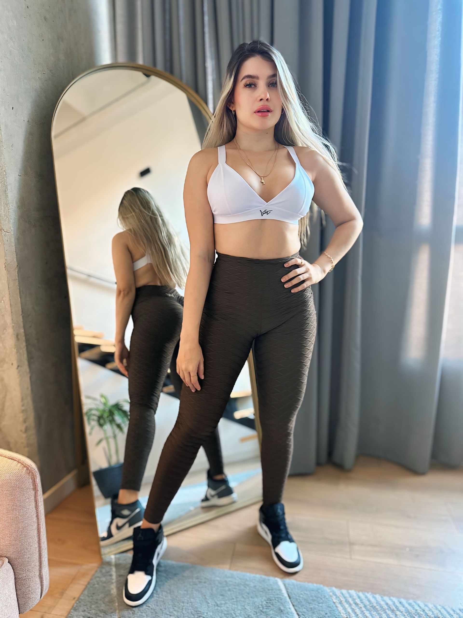 A woman is standing in front of a large mirror in a room.