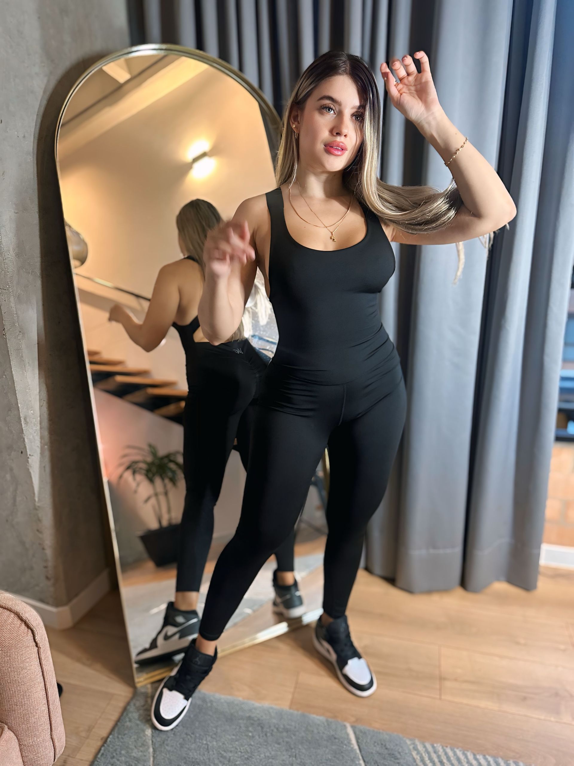 A woman is standing in front of a large mirror in a room.