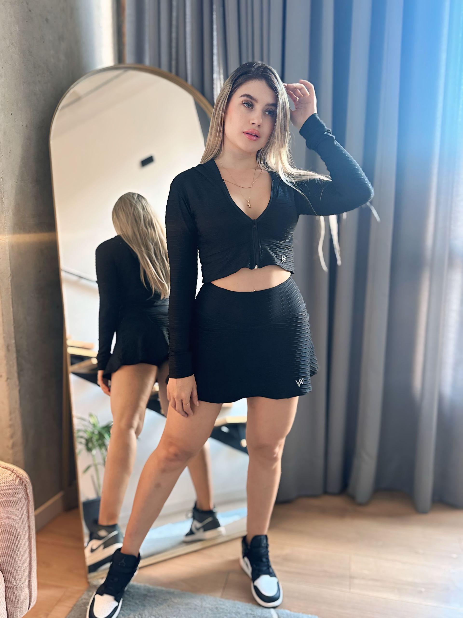 A woman in a black dress is standing in front of a mirror.