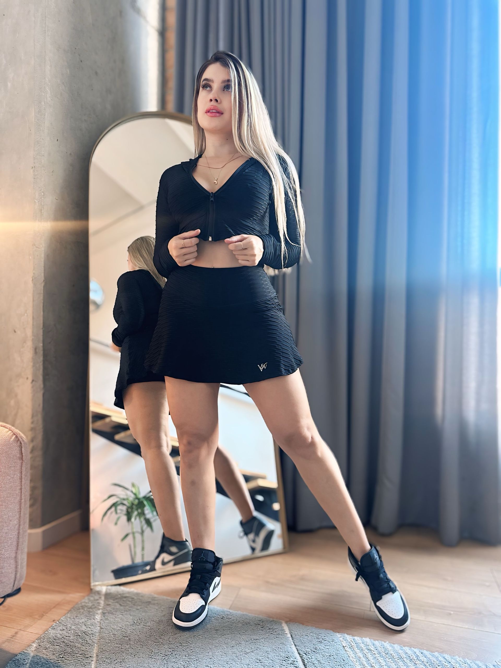 A woman is standing in front of a large mirror in a room.