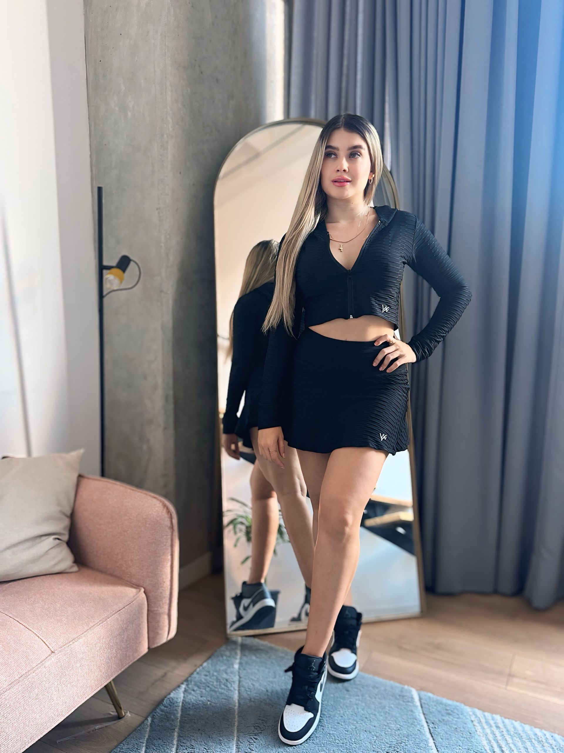 A woman is standing in front of a large mirror in a living room.