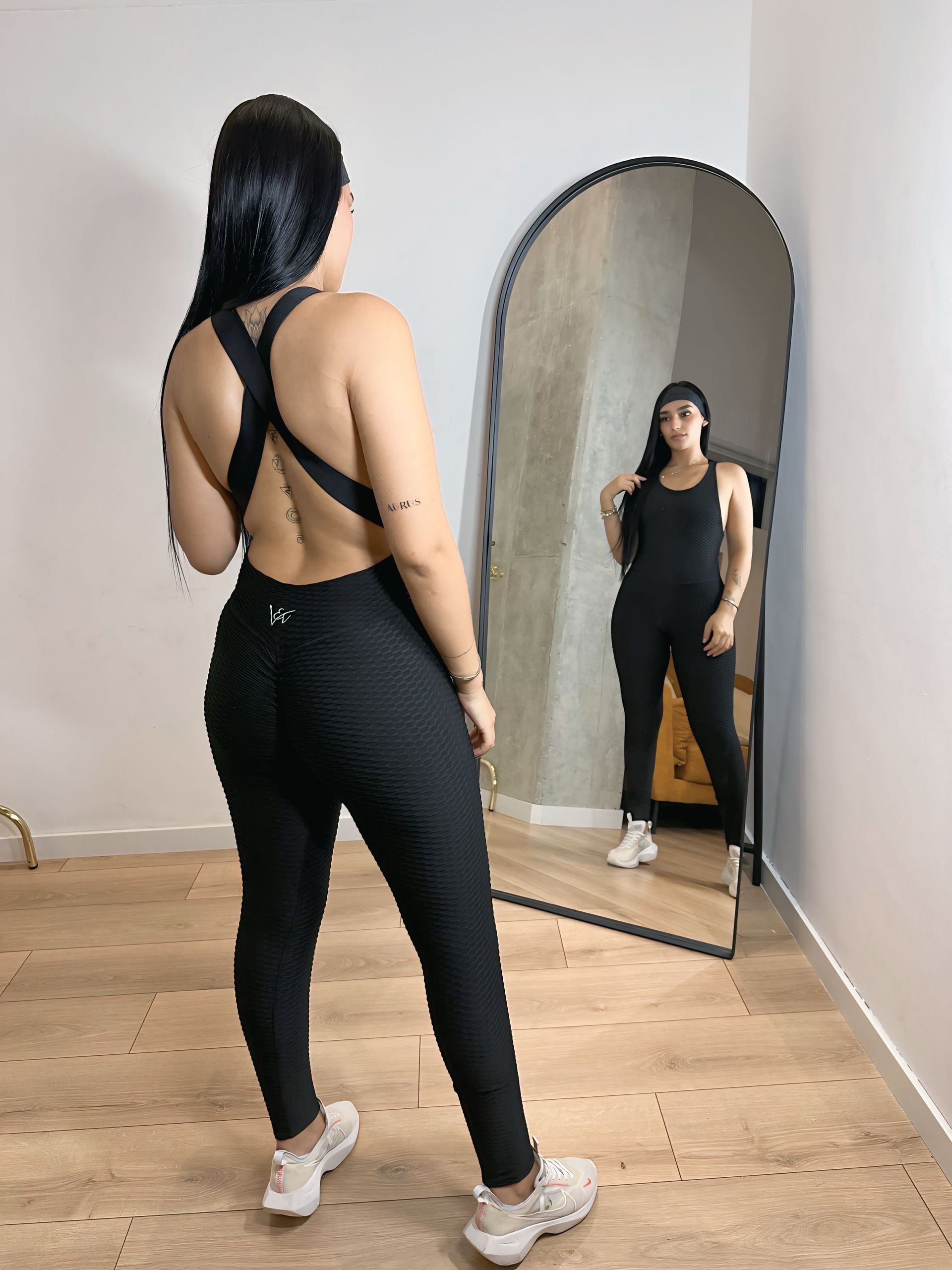 A woman in a black jumpsuit is standing in front of a mirror.